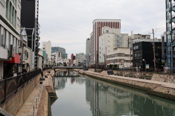 Serene view of a city canal in Fukuoka, Japan, flanked by modern architecture and reflective waters.