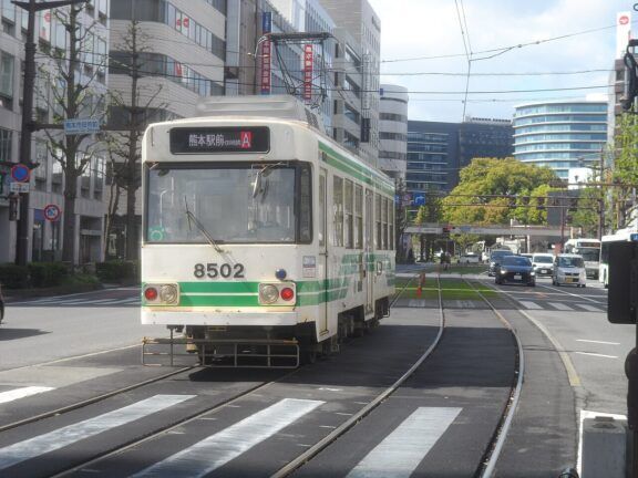 A picture of Kumamoto City Tram on the road during daytime